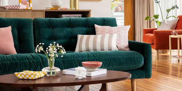 A living room with wooden coffee table, green sofa and grey and pink cushions on it.